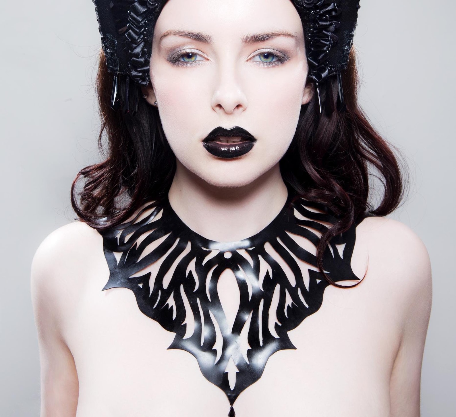 Gothic latex cutout collar in shiny black with teardrop bead, modeled on woman with dark hair and black lipstick.