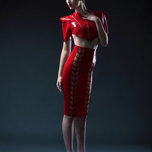 Pu&ograve; includere: Una donna indossa un top e una gonna in lattice rosso con un design geometrico. Il top ha un collo alto e una silhouette aderente. La gonna &egrave; una gonna a matita con vita alta e una silhouette aderente.