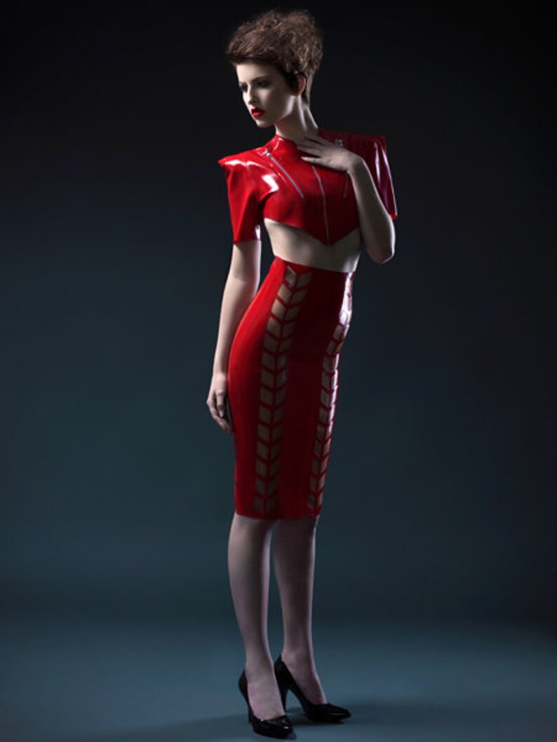 Pu&ograve; includere: Una donna indossa un top e una gonna in lattice rosso con un design geometrico. Il top ha un collo alto e una silhouette aderente. La gonna &egrave; una gonna a matita con vita alta e una silhouette aderente.