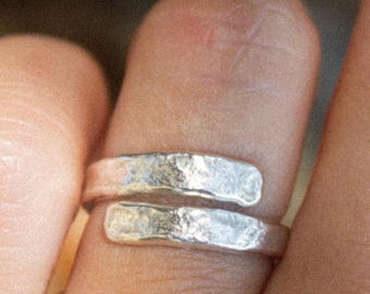 May include: A silver ring with a hammered texture. The ring is open and can be adjusted to fit different finger sizes.