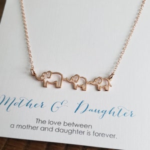 Puede incluir: Un collar de oro rosa con tres siluetas de elefantes conectadas. El collar est&aacute; sobre una tarjeta blanca con el texto "Madre e Hija. El amor entre una madre y su hija es para siempre."
