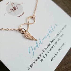 May include: Rose gold necklace featuring an infinity symbol and a wing charm. The necklace is displayed on a card with the word "Goddaughter" in script and the text "A goddaughter fills your heart with love and joy as if they were your very own."