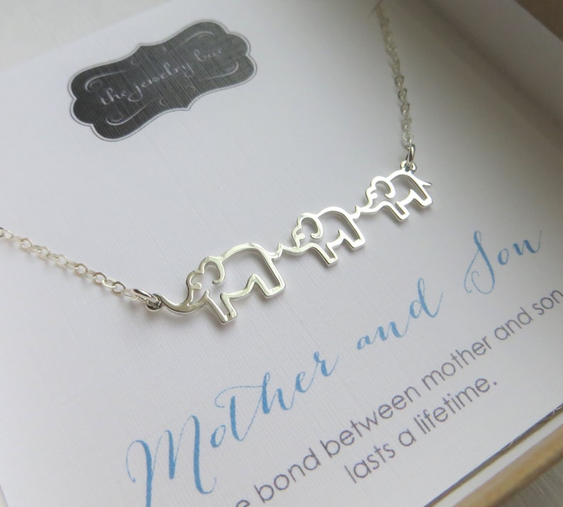 Puede incluir: Collar de plata con tres siluetas de elefantes conectadas. El collar est&aacute; en una caja con una tarjeta azul y blanca que dice "Madre e Hijo, el v&iacute;nculo entre madre e hijo dura toda la vida."