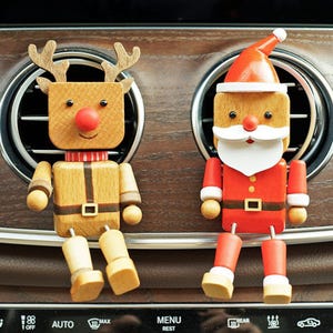 May include: Two wooden Christmas-themed car air vent decorations. One is a reindeer with antlers and a red nose, the other is Santa Claus with a red suit and hat. Both are made of wood and have a cartoonish design.