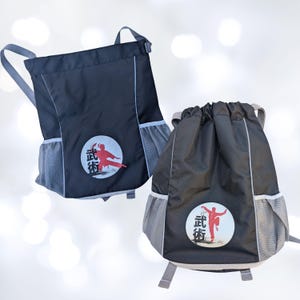 May include: Two black drawstring backpacks with gray accents and side pockets. Each backpack features a circular emblem with a red martial arts figure and Japanese characters. The backpacks have gray shoulder straps and a top handle.