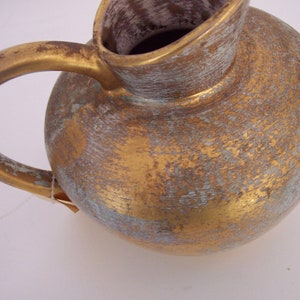 May include: A gold ceramic pitcher with a distressed finish. The pitcher has a round body and a curved handle.