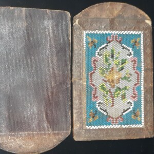 K&ouml;nnte beinhalten: Ein kleines, rechteckiges, braunes, ledergebundenes Buch mit einem perlenbesetzten Blumendesign auf dem vorderen Umschlag.