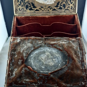 May include: An antique wooden box with a brass latch and a velvet lining. The box is open and the inside is visible. The velvet lining is worn and faded, and there is a hole in the centre of the box.