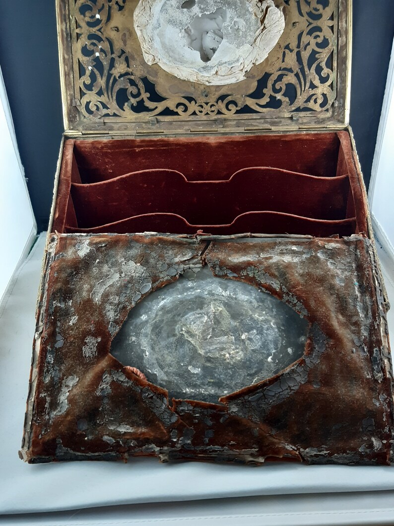 May include: An antique wooden box with a brass latch and a velvet lining. The box is open and the inside is visible. The velvet lining is worn and faded, and there is a hole in the centre of the box.
