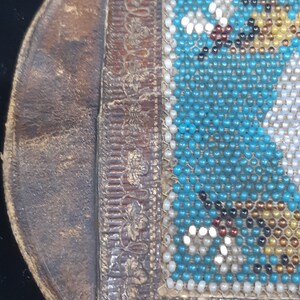 K&ouml;nnte beinhalten: Eine kleine braune Lederb&ouml;rse mit einem Perlenklappen. Die Perlen sind t&uuml;rkis, wei&szlig; und gold.