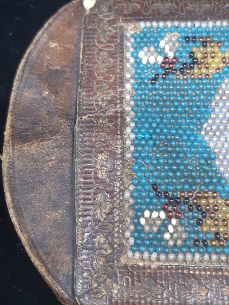 K&ouml;nnte beinhalten: Eine kleine braune Lederb&ouml;rse mit einem Perlenklappen. Die Perlen sind t&uuml;rkis, wei&szlig; und gold.