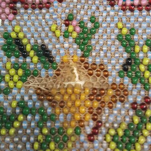 K&ouml;nnte beinhalten: Nahaufnahme eines Perlenmusters mit verschiedenen Farben, darunter Gr&uuml;n, Blau, Gelb, Rot und Wei&szlig;. Die Perlen sind in einem geometrischen Muster angeordnet.