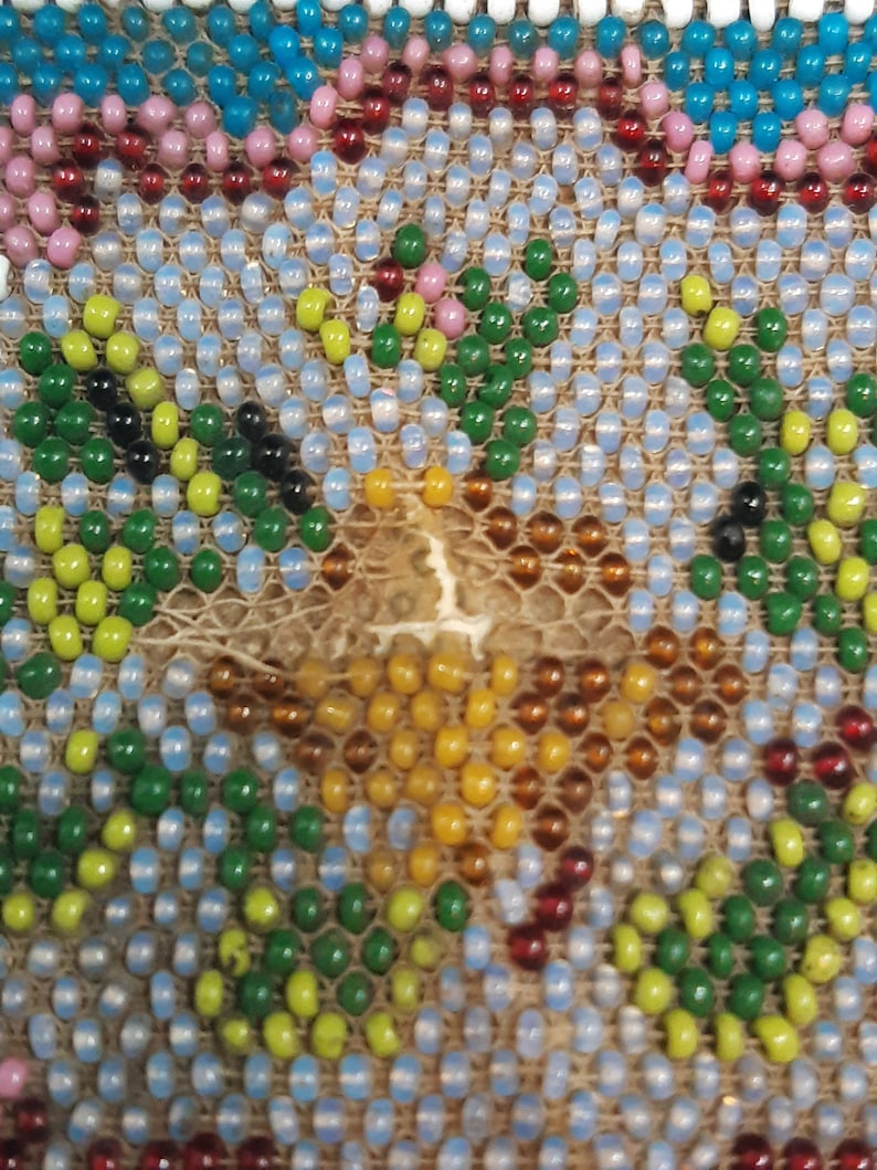 K&ouml;nnte beinhalten: Nahaufnahme eines Perlenmusters mit verschiedenen Farben, darunter Gr&uuml;n, Blau, Gelb, Rot und Wei&szlig;. Die Perlen sind in einem geometrischen Muster angeordnet.