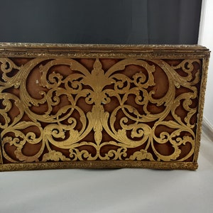 May include: A vintage gold-coloured metal box with a decorative, intricate, cut-out design. The box has a brown velvet lining.
