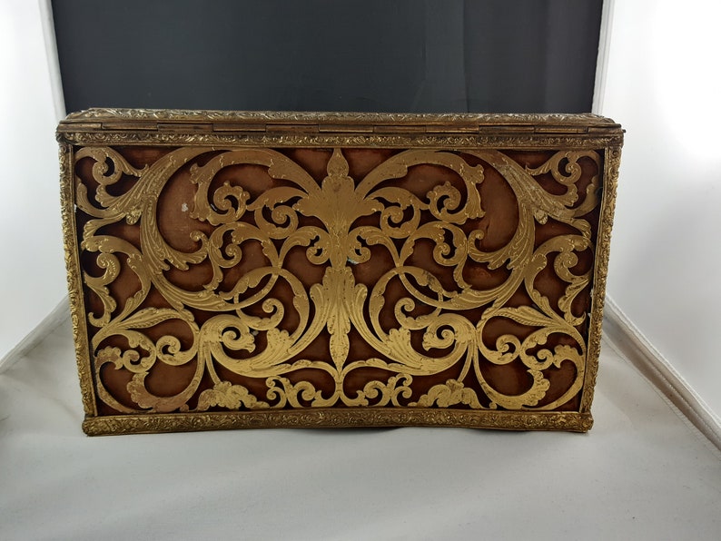 May include: A vintage gold-coloured metal box with a decorative, intricate, cut-out design. The box has a brown velvet lining.