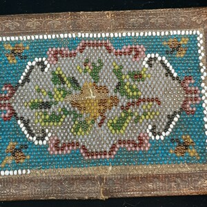 K&ouml;nnte beinhalten: Eine kleine, rechteckige Schachtel mit einem Perlenmuster. Die Schachtel ist aus braunem Leder und hat ein florales Muster in der Mitte. Die Perlen sind in verschiedenen Farben, darunter Wei&szlig;, Blau, Gr&uuml;n und Rot.