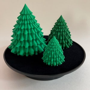 May include: Three green 3D printed Christmas trees of different sizes on a black rotating display stand.