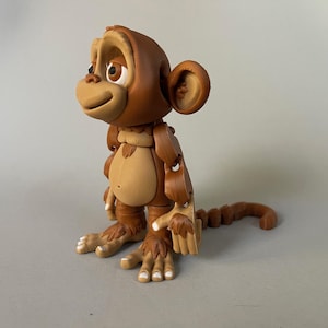 May include: A brown and tan articulated monkey toy with a jointed tail. The monkey has a friendly expression and large brown eyes.