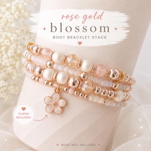 May include: A rose gold blossom boot bracelet stack featuring multiple strands of beads in shades of cream, white, and metallic rose gold. The bracelet includes a five-petaled flower charm and text that reads rose gold blossom BOOT BRACELET STACK.