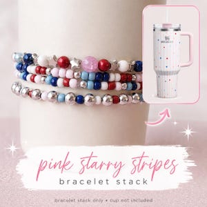 May include: A stack of beaded bracelets in red, white, blue, and silver. The bracelets are wrapped around a white cylindrical object. A pink and white striped tumbler with red and blue stars is in the background. Text reads "pink starry stripes bracelet stack."