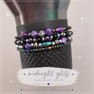 May include: A stack of beaded bracelets in shades of purple, black, and iridescent colors. The bracelets are displayed on a black textured surface. The text "midnight glitz bracelet stack" is visible.