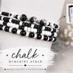 Könnte beinhalten: Ein Stapel Armbänder mit schwarzen, weißen und silbernen Perlen. Die Armbänder haben herzförmige Perlen und dekorative Kugeln. Das Bild zeigt auch einen weißen Becher mit Griff und dem Text "Stanley". Der Text "chalk bracelet stack" ist ebenfalls enthalten.