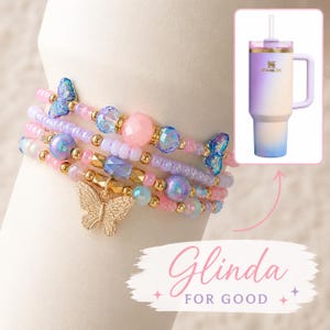 Könnte beinhalten: Mehrere Armbänder mit Perlen in Pastellfarben, mit Schmetterlingsanhängern und Perlen. Ein Stanley-Becher in einem Farbverlauf aus Lila, Weiß und Blau ist ebenfalls abgebildet. Der Text "Glinda FOR GOOD" steht unten.