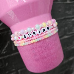 May include: Pink tumbler with a multi-layered beaded bracelet that says "I love spring".
