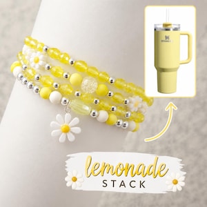 Könnte beinhalten: Ein Stapel aus Perlenarmbändern in Gelb-, Weiß- und Silbertönen, mit Gänseblümchen-Anhängern. Ein gelber Stanley-Becher mit Griff und Strohhalm ist in der Ecke abgebildet. Der Text "lemonade stack" ist darunter zu sehen.