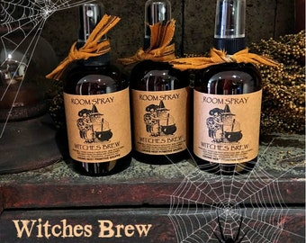 May include: Three dark brown spray bottles with brown labels that read "Room Spray" and "Witches Brew". Each bottle has a decorative orange ribbon tied around the neck. The image includes a spider web and the text "Witches Brew room spray".