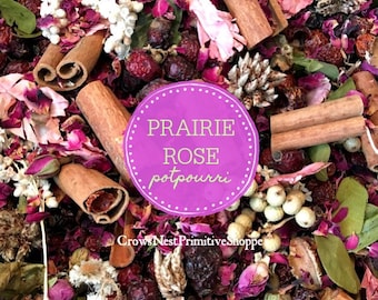 May include: A close-up of a purple and white potpourri mix with cinnamon sticks, dried rose petals, and other natural elements. The text "Prairie Rose potpourri" is written on a purple circle.