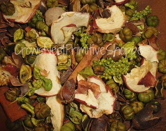 May include: A close-up of a mixture of dried fruit, spices, and greenery. The mixture includes apple slices, cinnamon sticks, and green leaves. The mixture is a popular scent for potpourri.