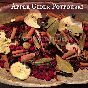 May include: Apple Cider Potpourri in a wooden bowl featuring dried apple slices, cinnamon sticks, green bay leaves, and small deep red berries. The text Apple Cider Potpourri is displayed at the top, with CrowsNestPrimitiveShoppe written below.