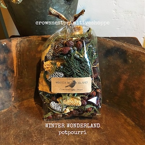 May include: A clear cellophane bag filled with potpourri, featuring pine cones, berries, and greenery. A label reads "WINTER WONDERLAND" and "Crow's Nest Primitive Shoppe". The bag is tied with a brown and tan ribbon.