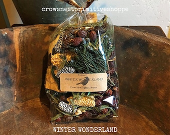 May include: A clear cellophane bag filled with potpourri, featuring pine cones, berries, and greenery. A label reads "WINTER WONDERLAND" and "Crow's Nest Primitive Shoppe". The bag is tied with a brown and tan ribbon.