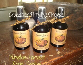 May include: Three brown glass bottles with black spray tops and black and yellow checkered ribbon tied around the necks. The bottles are labeled "Room Spray" and feature a pumpkin graphic. The text "Pumpkin Harvest Room Sprays" is written below the bottles.