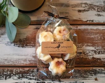 May include: A clear plastic bag filled with six white wax melts, labeled "Log Cabin natural soy melting tarts Crow's Nest Primitive Shoppe".