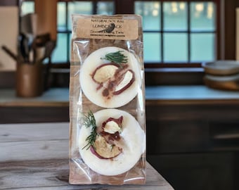 May include: Two round soy wax melts in a clear plastic bag. The melts are white with a brown and red apple slice on top. The bag has a label that reads "Natural Soy Wax Lumberjack Scents of the Forest"