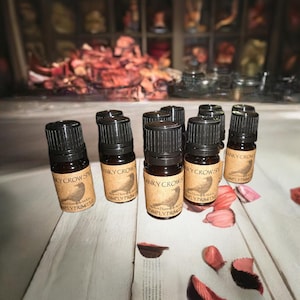 May include: A collection of small, brown glass bottles with black caps. Each bottle has a label with the text "ANKY CROW" and a bird illustration. The bottles are arranged on a white wooden surface with scattered petals.