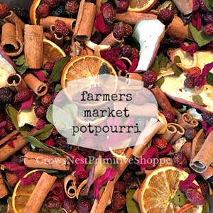May include: A close-up of a bowl filled with a variety of dried fruits, spices, and flowers. The mixture includes orange slices, cinnamon sticks, dried rose petals, and berries. The text "farmers market potpourri" is written on a white label.
