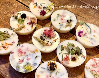 May include: Assortment of round, white soy wax melts with dried flowers and herbs embedded in the wax. The wax melts are arranged on a wooden surface. The text "CrowsNestPrimitiveShoppe" is visible in the top right corner of the image.