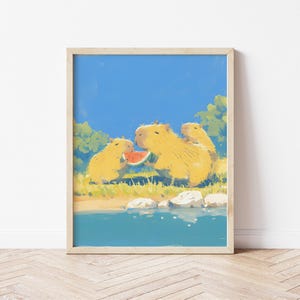 May include: A framed art print featuring a digital illustration of three golden-yellow capybaras sitting by a blue body of water. The capybaras are eating a slice of red watermelon. The scene includes green foliage, white rocks, and a blue sky.