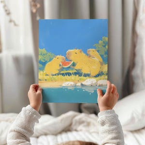 May include: A rectangular art print featuring a digital illustration of three golden-yellow capybaras standing near a blue body of water. The central capybara holds a slice of red watermelon, while green trees and a bright blue sky fill the background.