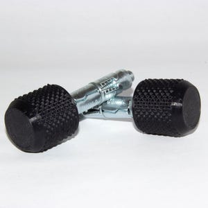 Könnte beinhalten: Zwei schwarze Kunststoff- und Metall-Dübel mit einer strukturierten Oberfläche. Die Dübel sind für die Verwendung in Trockenbauwänden oder anderen weichen Materialien konzipiert.