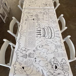 May include: A long white paper coloring table runner featuring black line art illustrations of Sesame Street characters, birthday cakes, balloons, and gift boxes. The text OREOLUWA STREET is printed on a sign graphic on the paper surface.