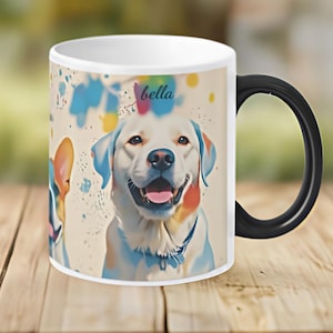 May include: White ceramic mug with a black handle. The mug features a colourful illustration of two dogs, one with the name "bella" printed on the mug. The background is a light beige with colourful paint splatters.