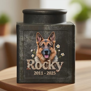 Peut inclure: Urne fun&eacute;raire pour animaux de compagnie de couleur gris fonc&eacute;, orn&eacute;e d'un portrait de berger allemand et de fleurs blanches. Le nom "Rocky" et les ann&eacute;es "2011-2025" sont affich&eacute;s, cr&eacute;ant un souvenir personnalis&eacute;.
