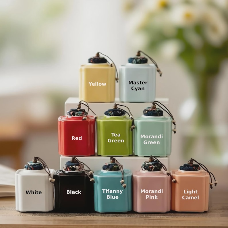 May include: A collection of ten colorful ceramic tea canisters. Each canister is square with a rounded top and a decorative lid. Colors include yellow, light blue, red, green, white, black, Tiffany blue, pink, and light camel. Text labels identify each color.