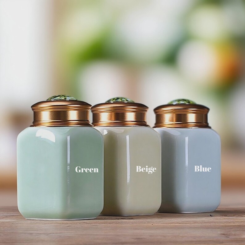 May include: Three ceramic jars in green, beige, and blue, each with a gold-colored lid and a decorative green gem on top. The jars are labeled "Green", "Beige", and "Blue" in white text.