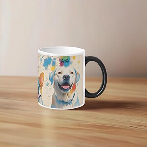 May include: White ceramic mug with a black handle. The mug features a colourful illustration of two dogs, one with the name "bella" written above it. The background is a light beige with colourful paint splatters.